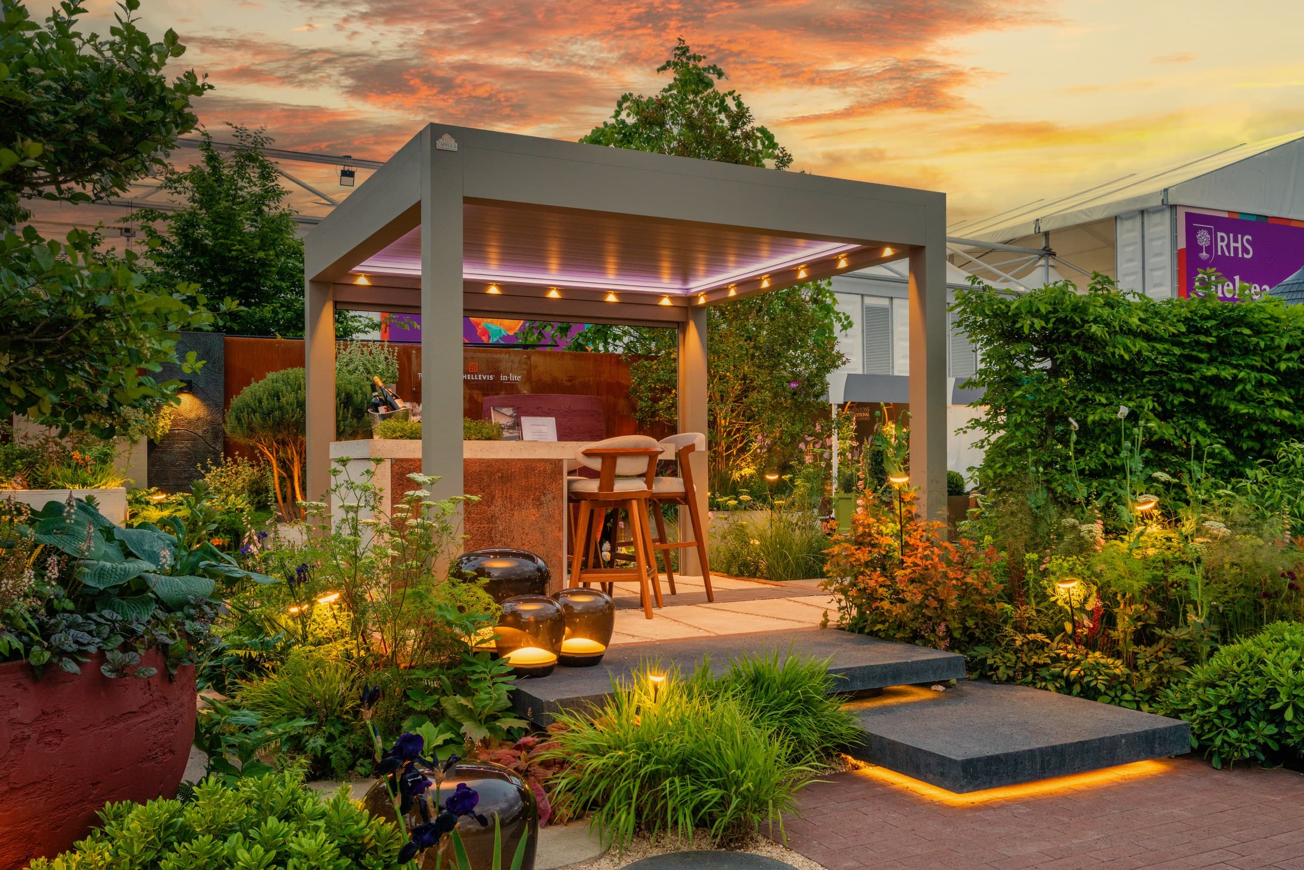 Ottorigo bioclimatic pergola with its aluminium louvred roof retracting over a garden lounge at sunset